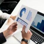 Analyse de graphiques business sur ordinateur et papier par une équipe en réunion.